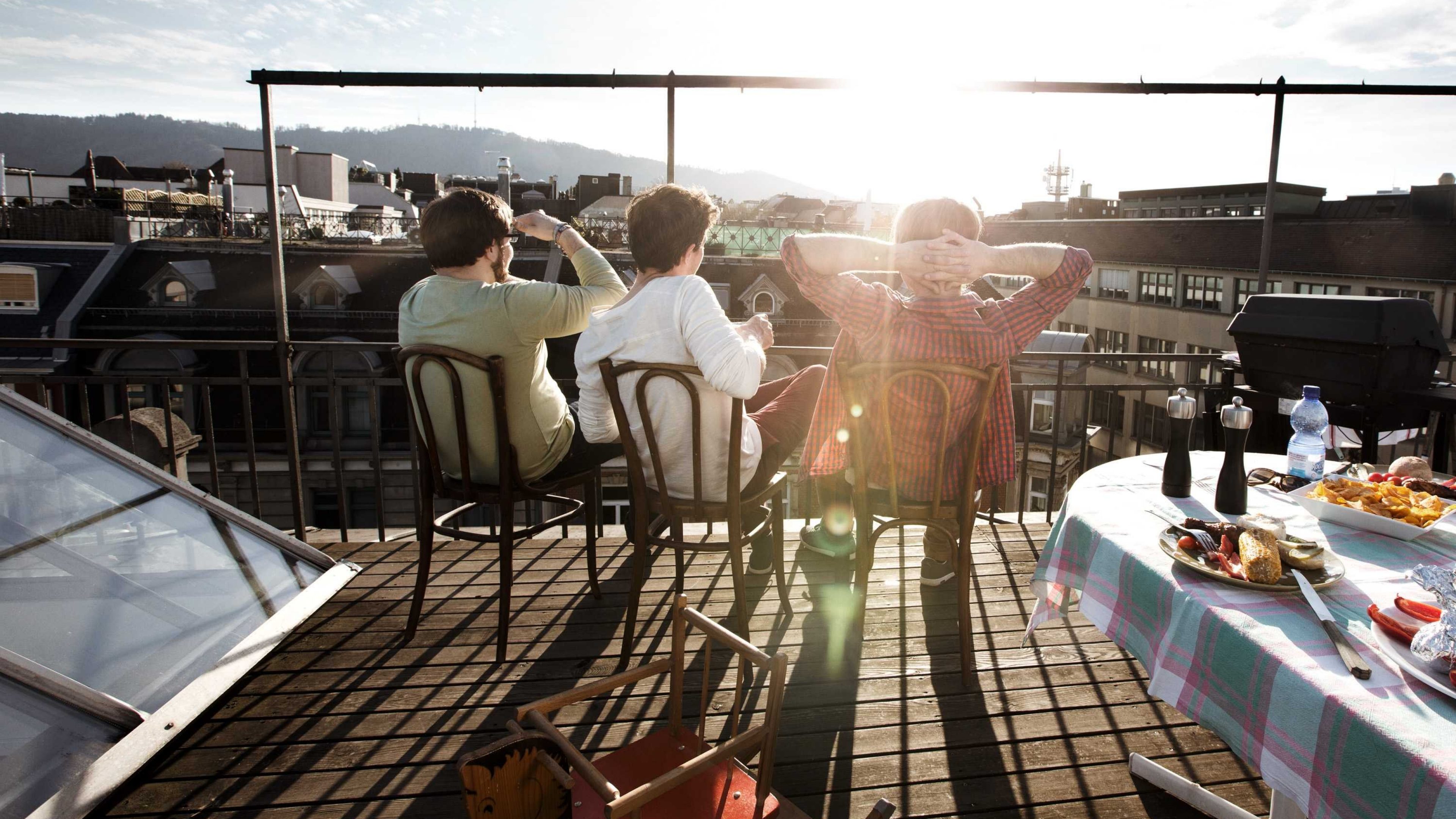 Menschen sitzen auf einer Dachterrasse und blicken in die Ferne.