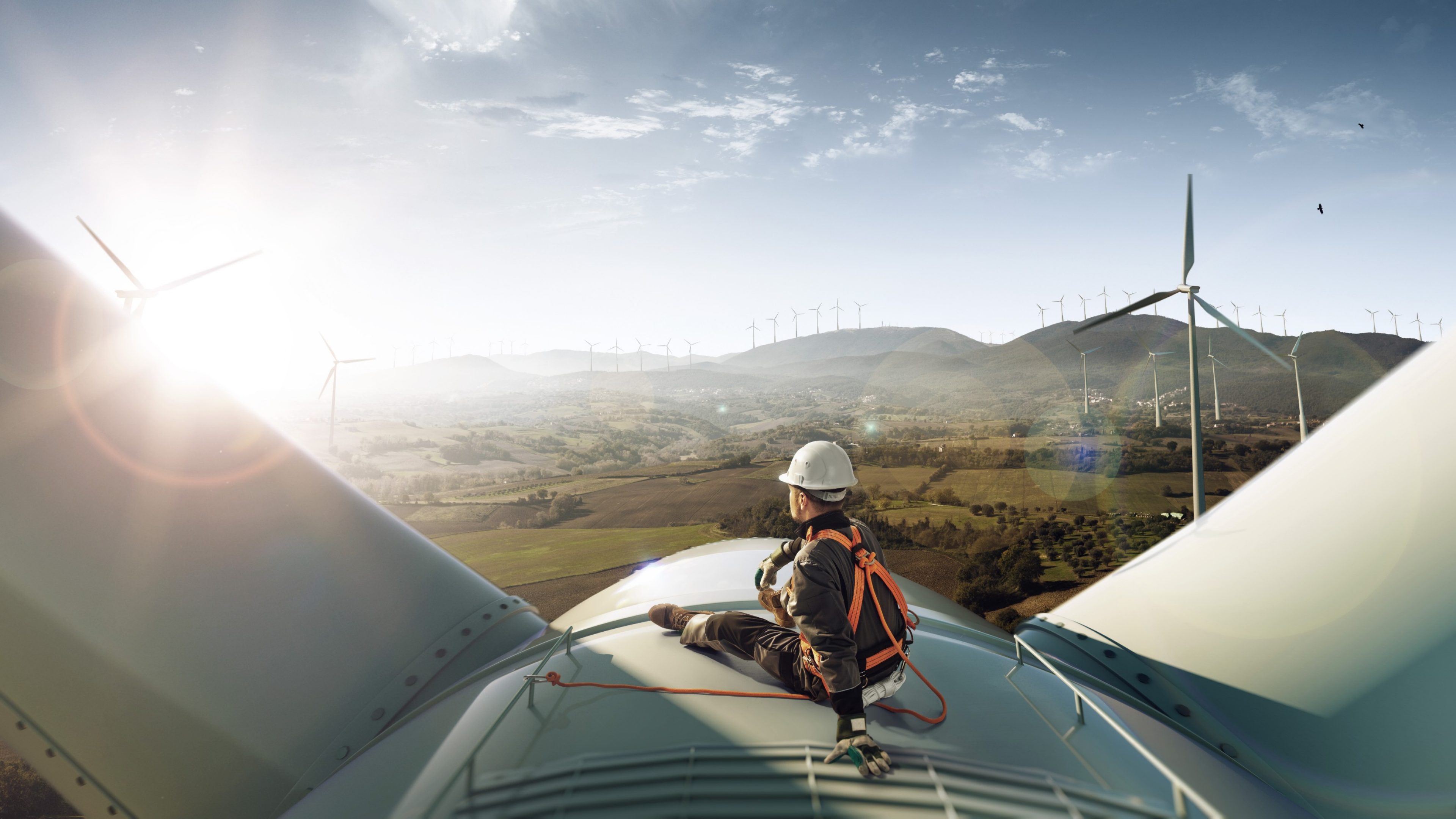 Happy engineer feel success after good work. He standing a top of windmill and looking beautiful sunset landscape