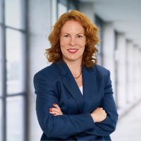 A photo of a woman standing in the Swiss Life Asset Managers building with her arms crossed and a smile on her face.
