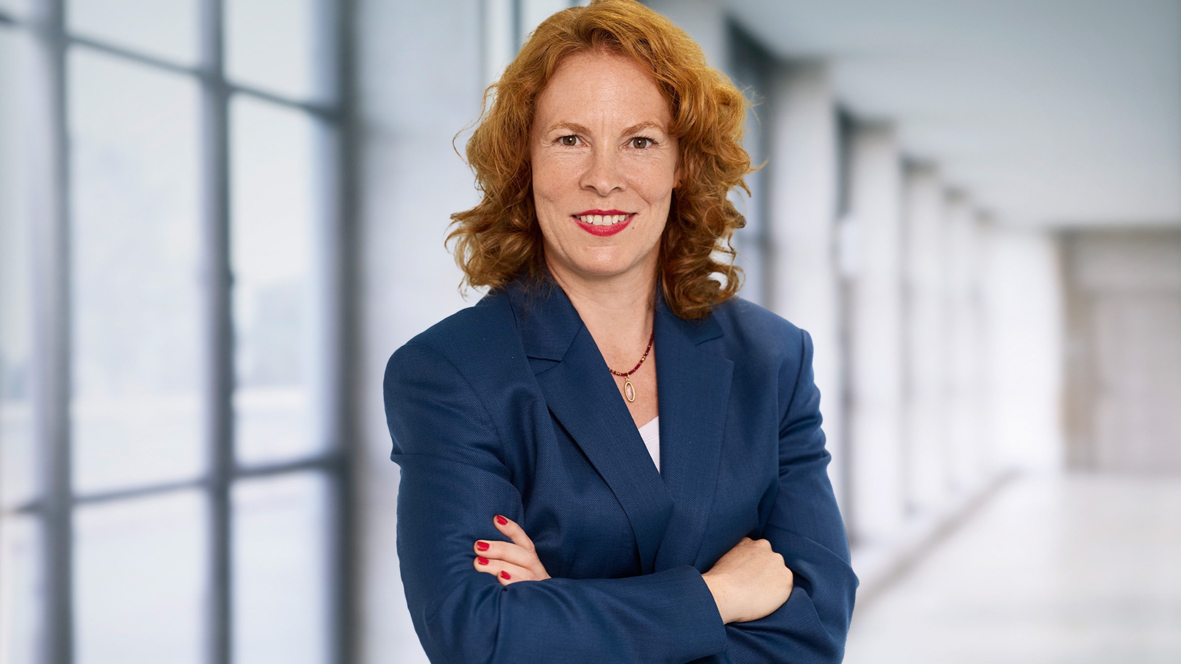 A photo of a woman standing in the Swiss Life Asset Managers building with her arms crossed and a smile on her face.