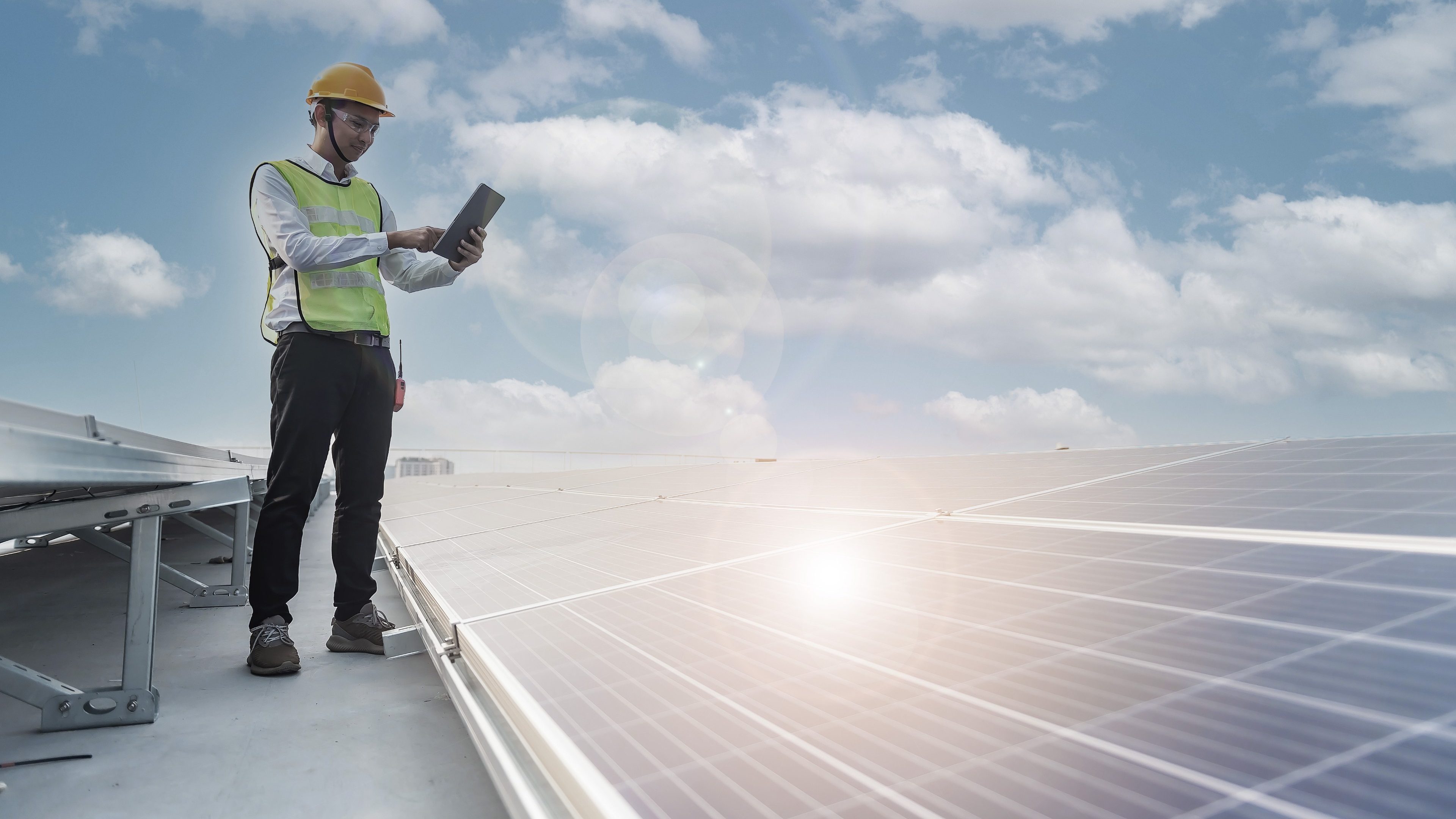 A man wearing a helmet and a high-visibility vest on the roof of a house, checking the solar panels.