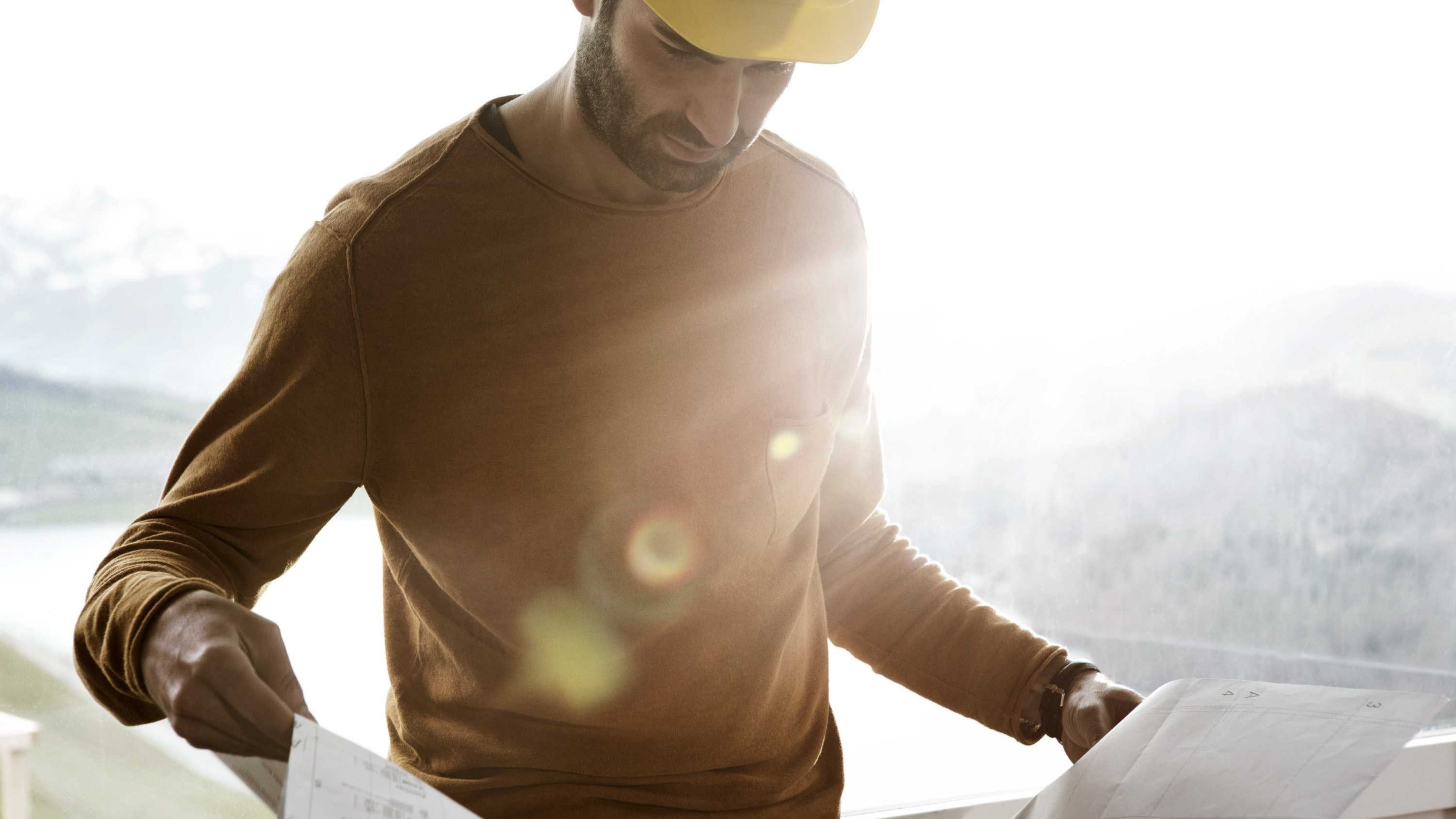 A man wearing a hard hat and looking at a construction plan.