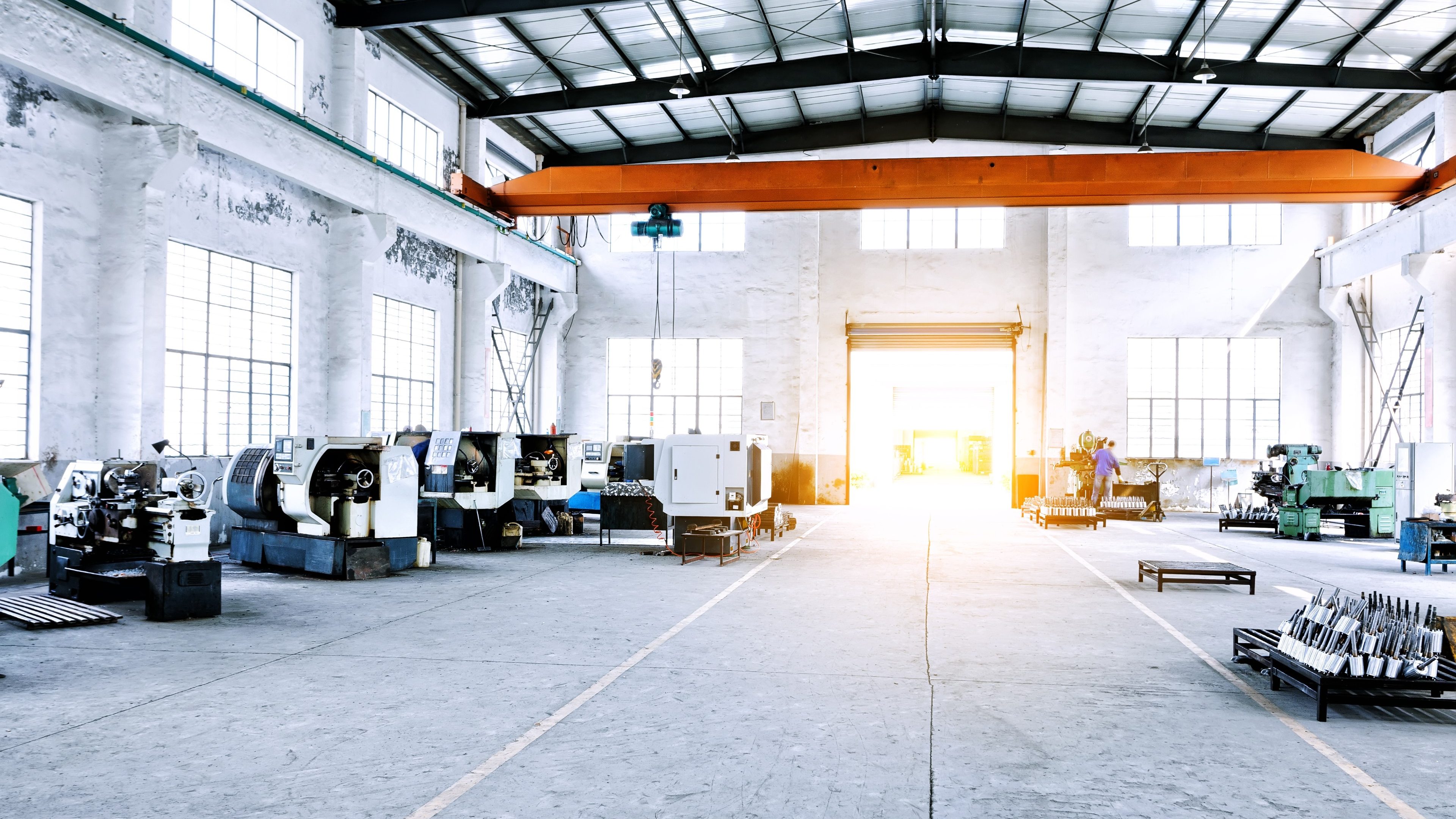 Grand hangar industriel baigné de lumière, avec des machines, sur certaines desquelles des personnes travaillent.