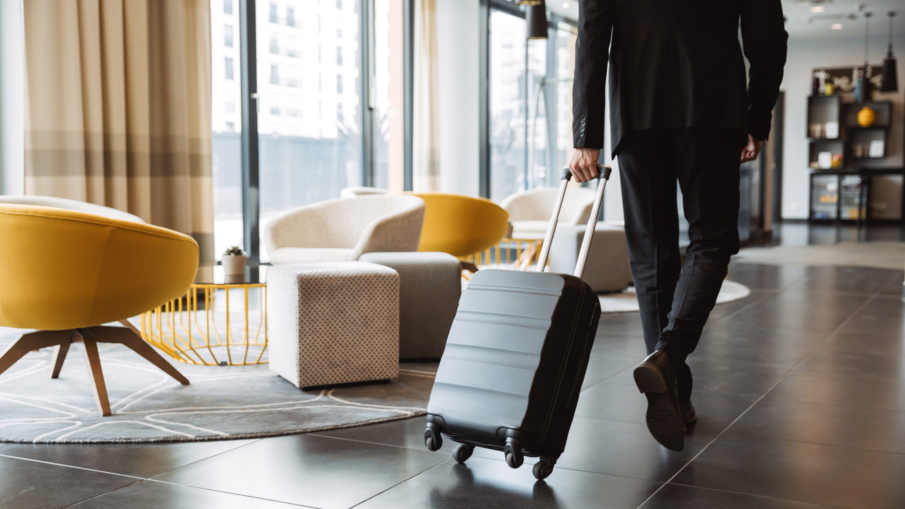Un homme avec une valise roulante qui entre dans un hall d’hôtel.