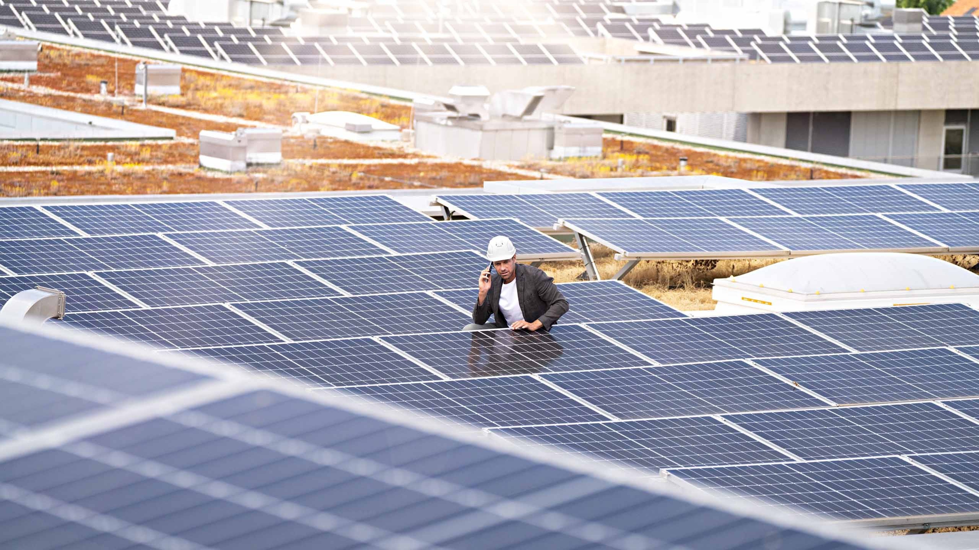 Un homme debout sur le toit d'une maison équipée de panneaux solaires.