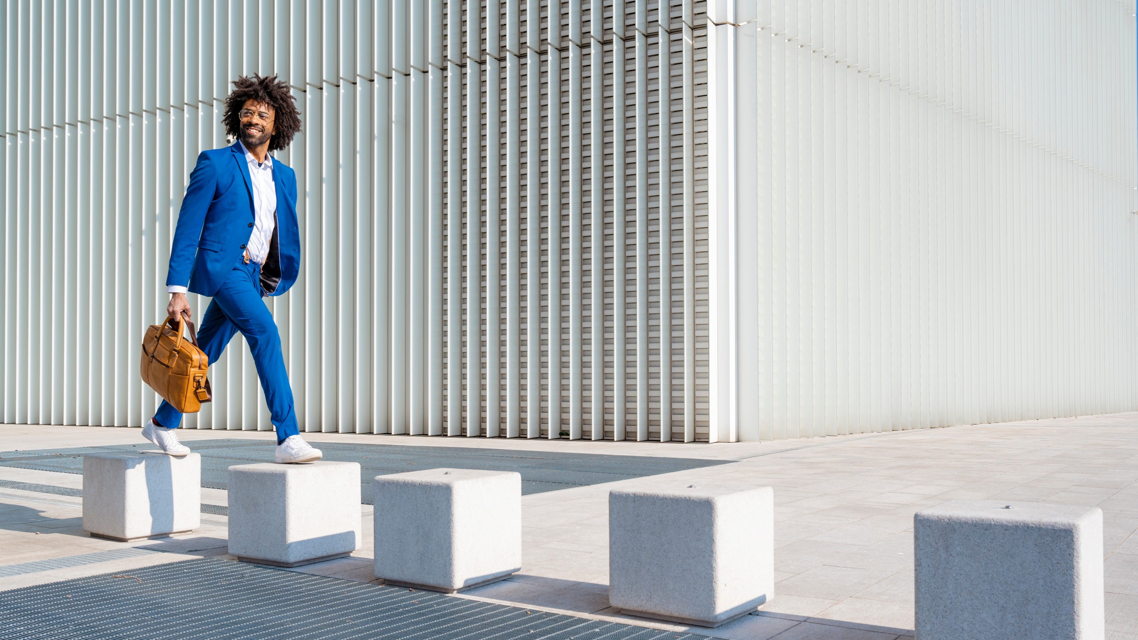 Happy businessman holding shoulder bag walking on concrete block